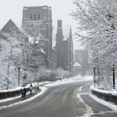 Students cross the College Avenue Stone Arch Bridge in winter, with a view of Myron Taylor Hall.