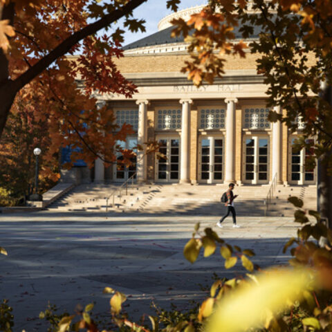 A student traverses Bailey Plaza amid fall foliage.