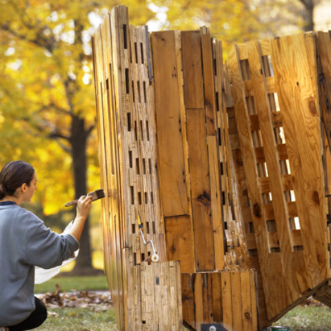 A teaching associate applies a coat of sealer to a sculpture by Leslie Lok as part of a Cornell Council for the Arts installation on the Arts Quad.