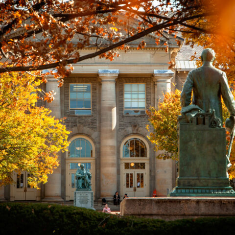Calm autumn scene of a Cornell building with a statue of Ezra Cornell in the foreground.